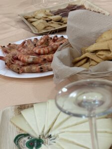 Shrimp on a white plate with crackers and sliced cheese arranged on a beige table.