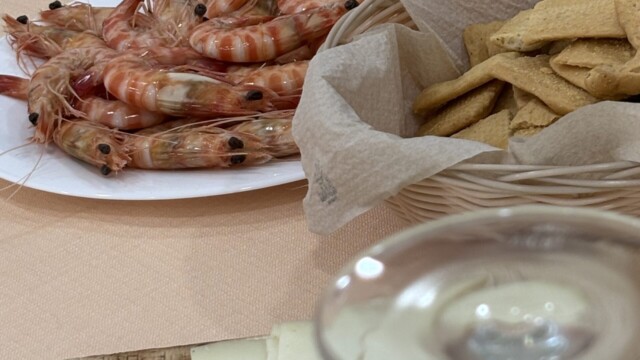 Shrimp on a white plate with crackers and sliced cheese arranged on a beige table.