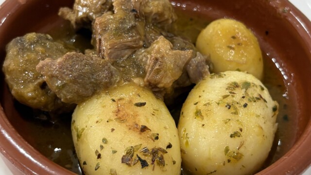 Braised beef and potatoes in a herb-garnished broth served in a terracotta pot.